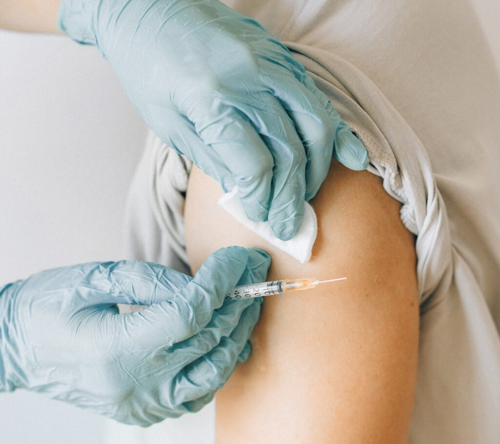 Hands with gloves with an injection needle, preparing to inject a fluid into a patient.